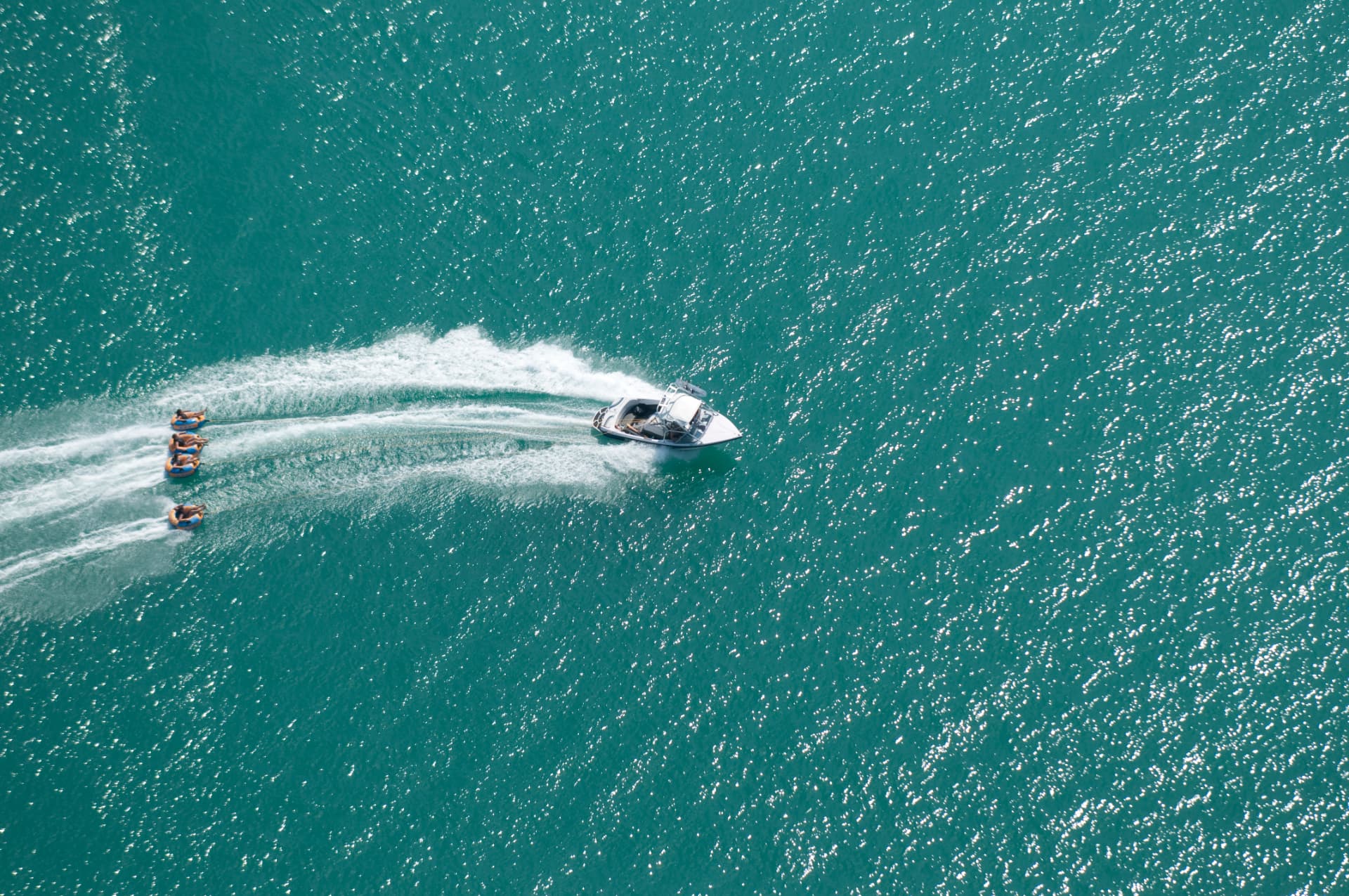 Aerial view of a speedboat pulling inflatable tubes across turquoise Lake Wörthersee