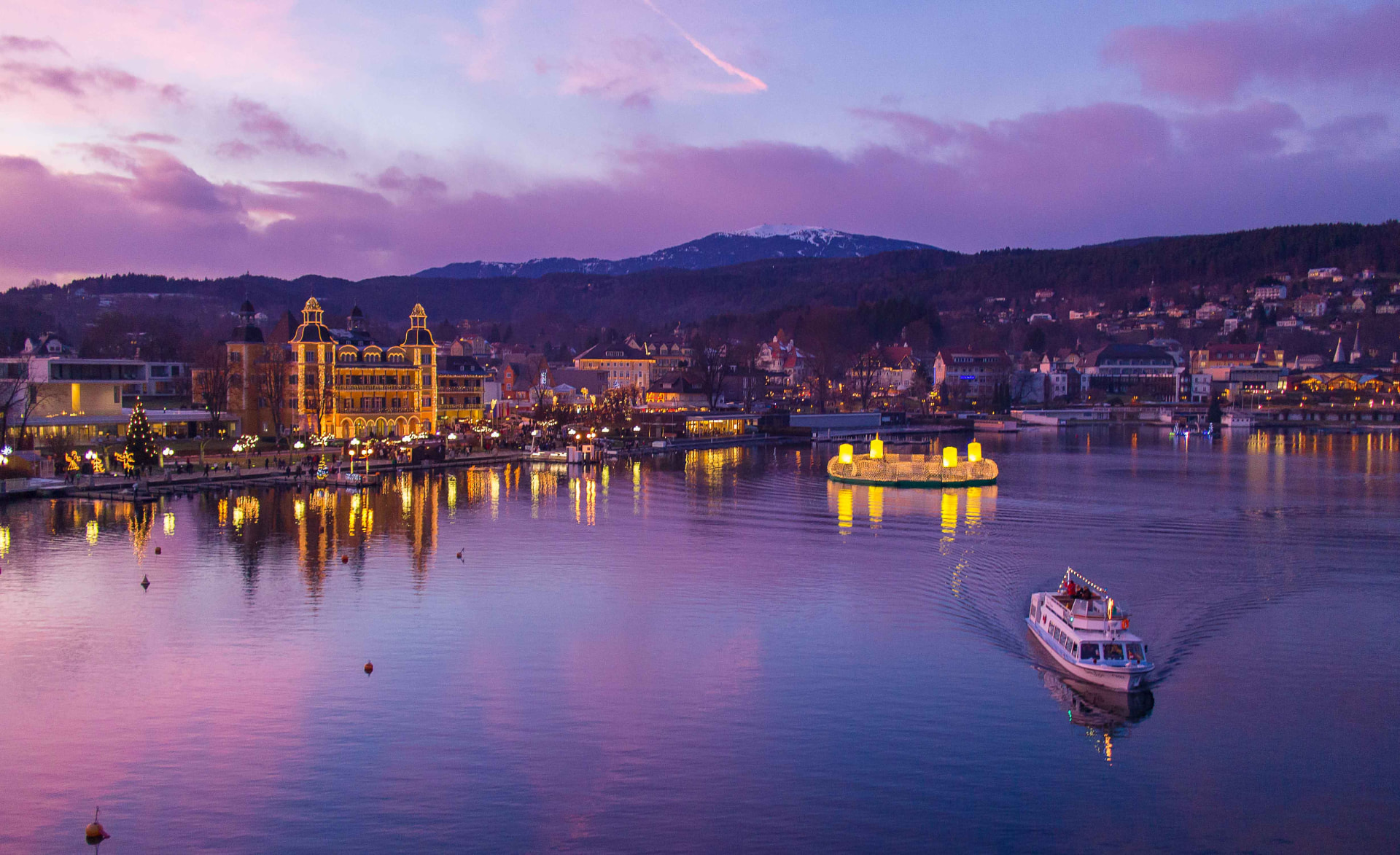 Evening lights reflecting on Lake Wörthersee with a passenger boat at dusk
