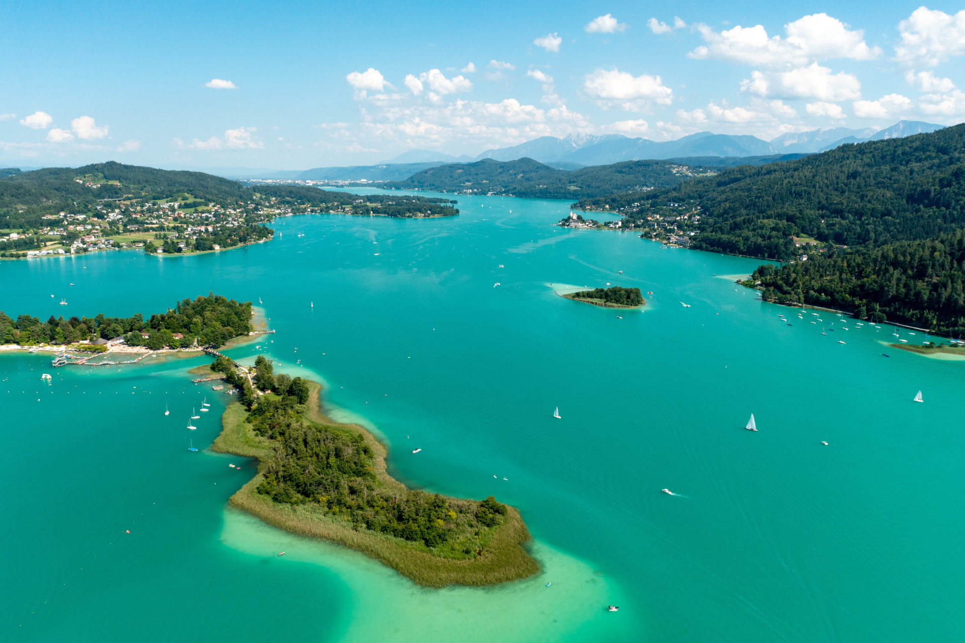 Aerial panorama of Lake Wörthersee with wooded islands, sailboats and turquoise shallows