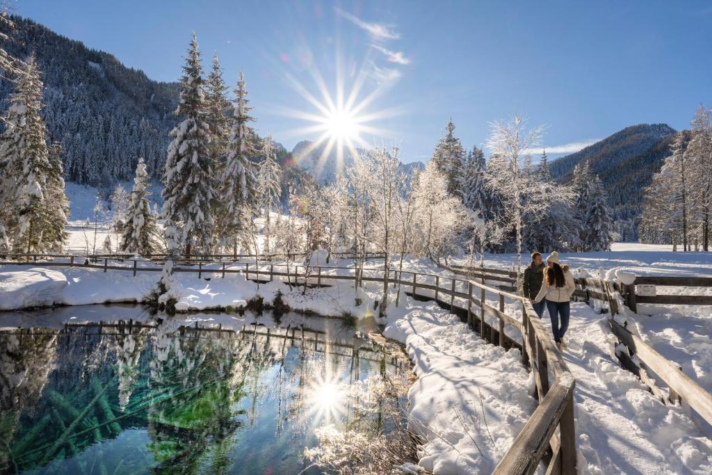 Snowy winter landscape with a turquoise stream, wooden footbridge and winter sun